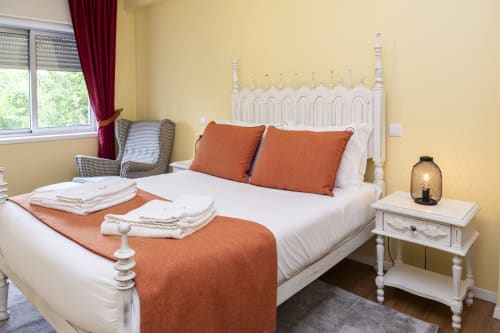 Quarto amarelo brilhante no RH Charming Apartments Braga com cama branca, almofadas laranja, criado-mudo e poltrona