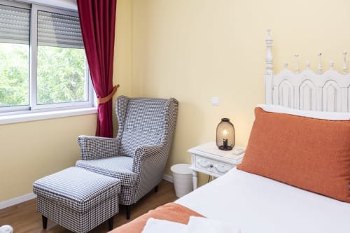Quarto luminoso em RH Charming Apartments em Braga com poltrona xadrez, cabeceira branca e almofada laranja