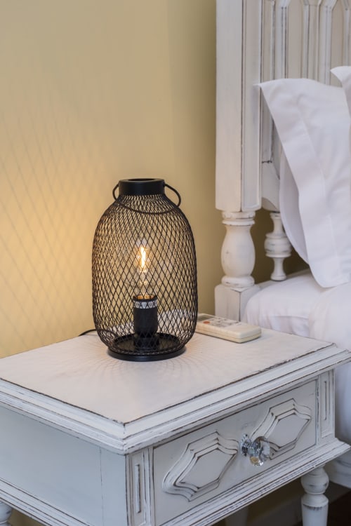 Lanterna de malha preta com vela em criado branco no quarto de hotel em Braga