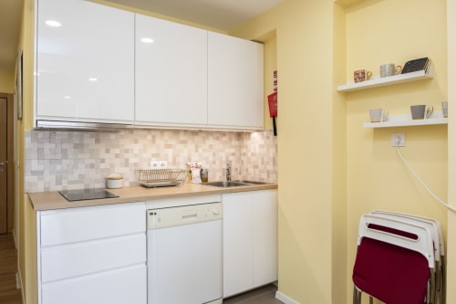 Cozinha moderna com armários brancos, azulejos bege, bancada de madeira e prateleiras abertas no RH Charming Apartments em Braga