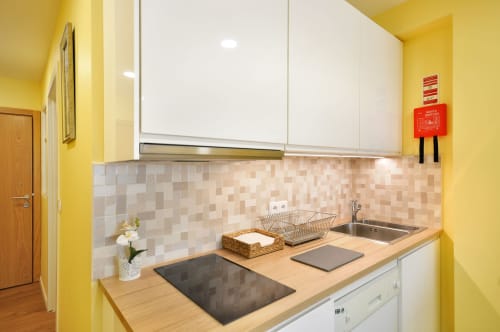 Cozinha amarelo vibrante no RH Charming Apartments, Braga com armários brancos, bancada de madeira e painel traseiro em azulejo bege.