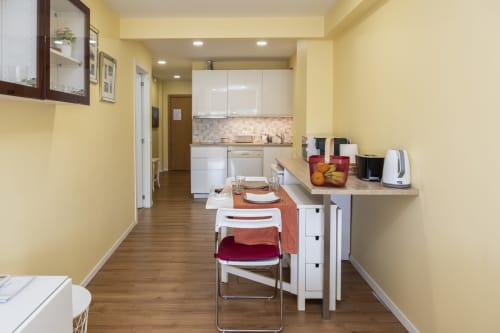 Área moderna de cozinha-sala de jantar em RH Charming Apartments em Braga com paredes amarelas, armários brancos e mesa de jantar vermelha