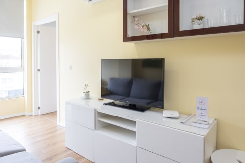 Moderna sala de estar em RH Charming Apartments Braga com paredes amarelas, TV de tela plana, unidade branca de entretenimento e