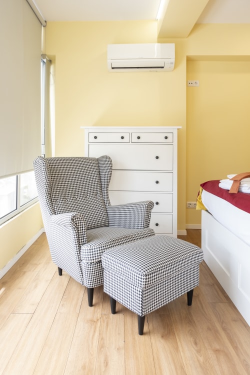 Quarto aconchegante no RH Charming Apartments em Braga com poltrona xadrez, cômoda branca e paredes amarelas.