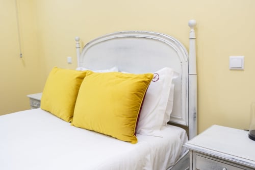 Quarto luminoso com almofadas amarelas na cama branca e cabeceira cinza nos RH Charming Apartments em Braga