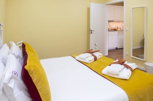 Quarto amarelo vibrante no RH Charming Apartments em Braga com cama branca, detalhes em amarelo e cozinha integrada visível