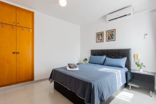 Moderno dormitorio en Haus Holiday Homes de San Pedro del Pinatar con ropa de cama azul, cabecero negro, armario de madera y aire acondicionado