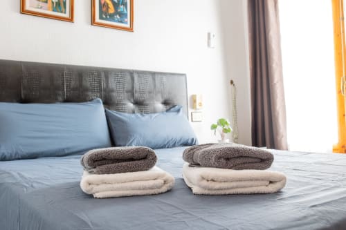 Habitación de huéspedes en Haus Holiday Homes con toallas dobladas sobre cama azul, cabecera oscura y cuadros en San Pedro del