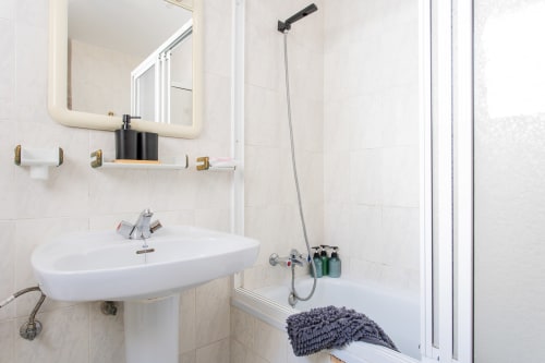 Baño moderno con lavabo blanco, espejo iluminado, accesorios dorados y área de ducha en Haus Holiday Homes, San Pedro del