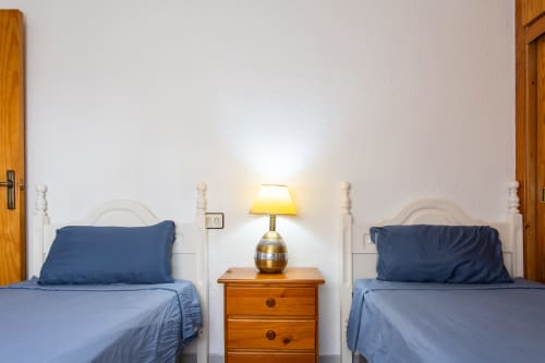 Habitación doble con ropa de cama azul, mesilla de noche de madera con lámpara en Haus Holiday Homes, San Pedro del Pinatar