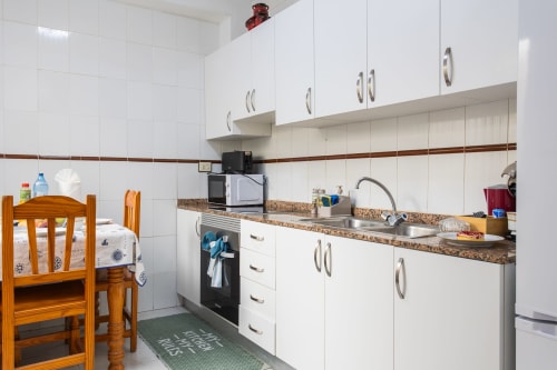 Cocina luminosa en Casa Bibaziz, San Pedro del Pinatar, con muebles blancos, encimera de granito y silla de madera
