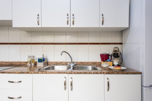 Cocina moderna con gabinetes blancos, encimera de corcho y fregadero doble de acero inoxidable en Haus Holiday Homes, San Pedro del