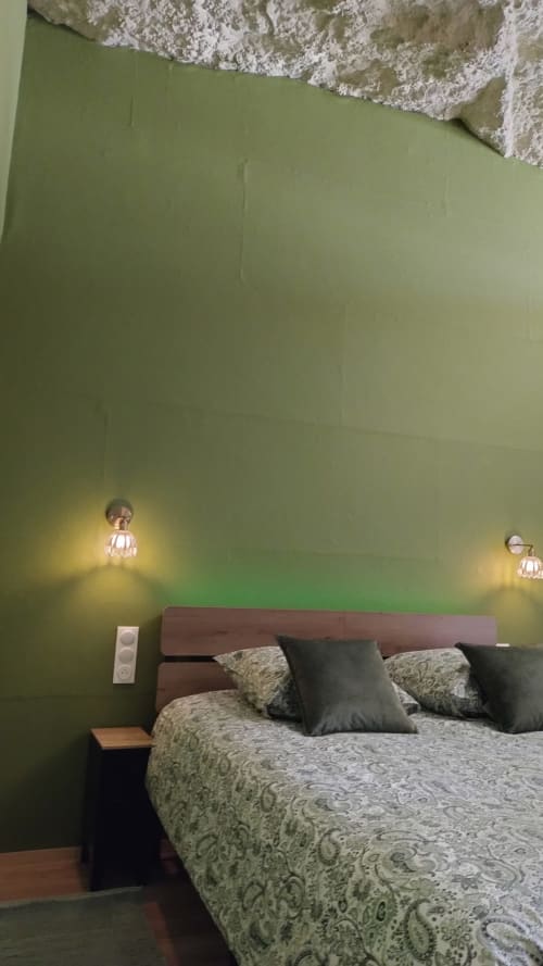 Chambre des Troglos de Beaulieu aux murs vert sauge, lit en bois, linge de lit motifs et éclairages d'ambiance