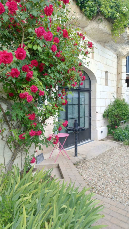 Des roses magenta éclatantes encadrent l'entrée voûtée d'un bâtiment en pierre aux Troglos de Beaulieu, un hôtel