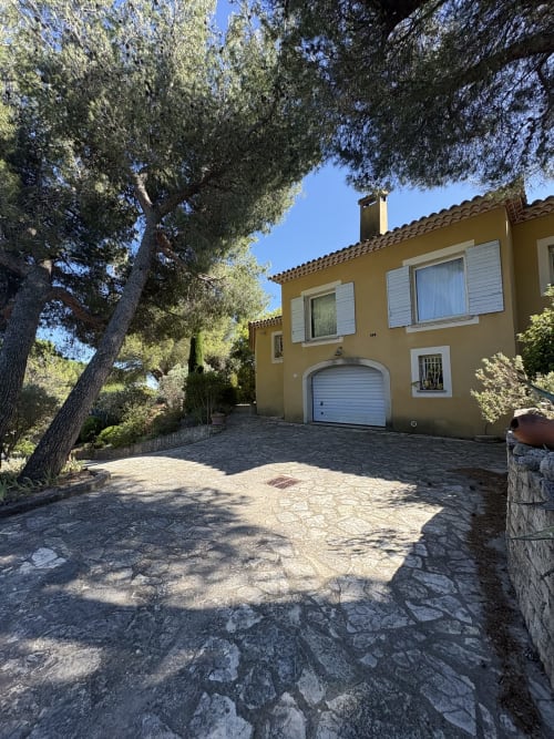 Villa jaune aux volets blancs avec garage à la Conciergerie Maurin à Arles, entourée d'arbres méditerranéens par beau temps