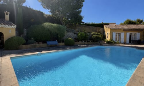Piscine de la Conciergerie Maurin à Arles, bâtiments jaunes et jardins paysagés sous un ciel bleu dégagé