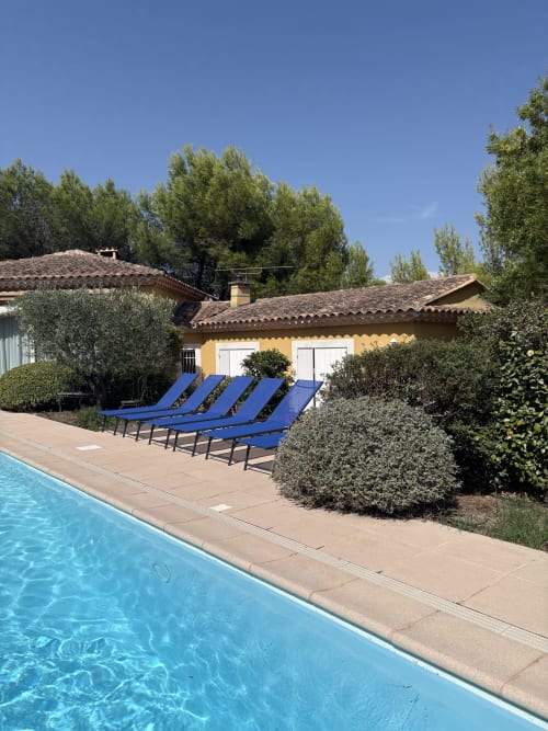 Piscine et chaises longues bleues de l'hôtel Conciergerie Maurin à Arles, bâtiment en pierre jaune et jardins méditerranéens