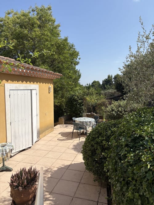 Terrasse ensoleillée à la Conciergerie Maurin à Arles : villa jaune, portes blanches, table à manger et jardins méditerranéens luxuriants