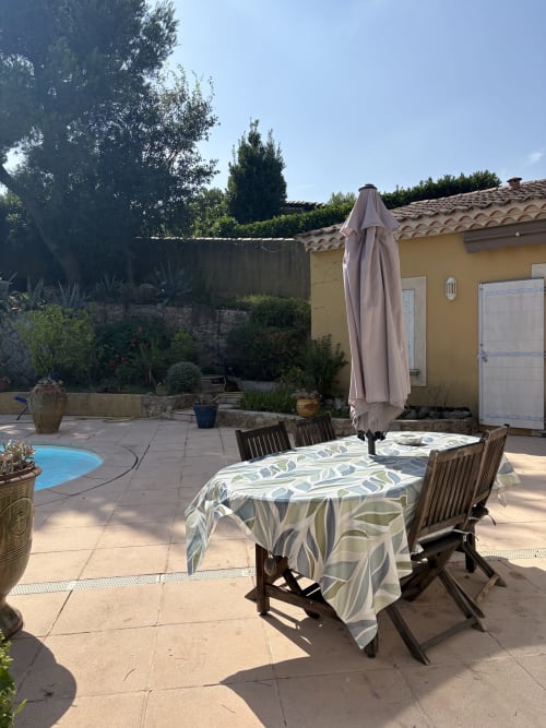 Espace repas extérieur à la Conciergerie Maurin à Arles avec table de patio, parasol, chaises en bois et vue sur la piscine