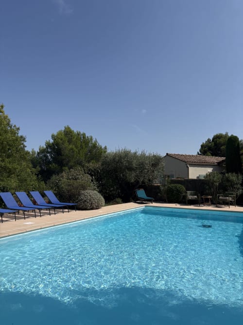 Piscine cristalline à la Conciergerie Maurin à Arles avec transats bleus, terrasse et vue sur la villa campagnarde