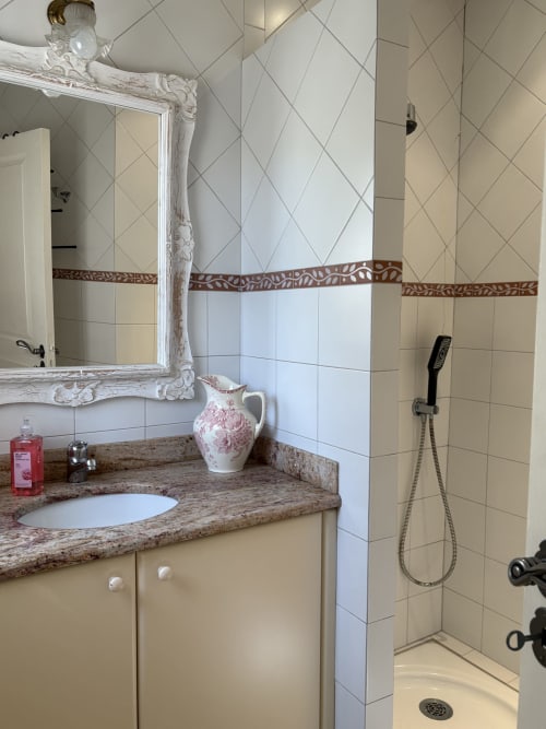 Salle de bain élégante de la Conciergerie Maurin à Arles avec vasque en granit, miroir blanc orné et douche carrelée