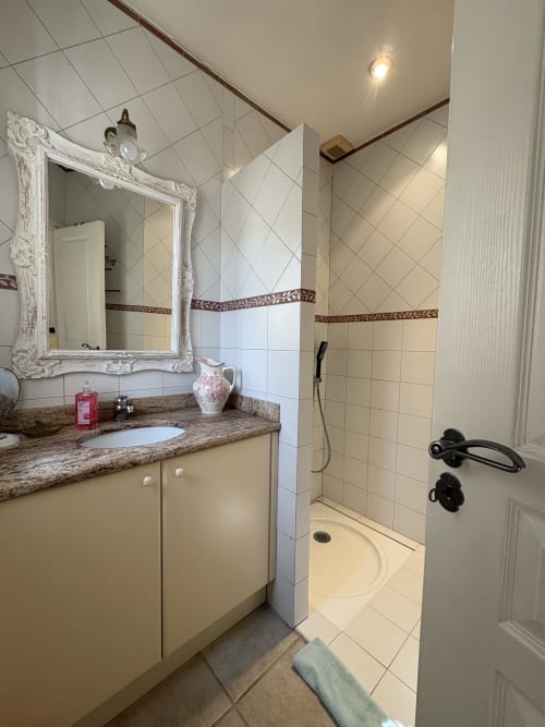Salle de bains moderne à la Conciergerie Maurin à Arles, avec plan de travail en granit, miroir cadre blanc, douche à l'italienne et teintes crème