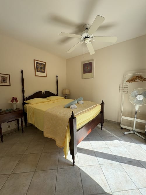Chambre avec literie jaune, lit à baldaquin en bois foncé, ventilateur de plafond et carrelage à la Conciergerie Maurin d'Arles