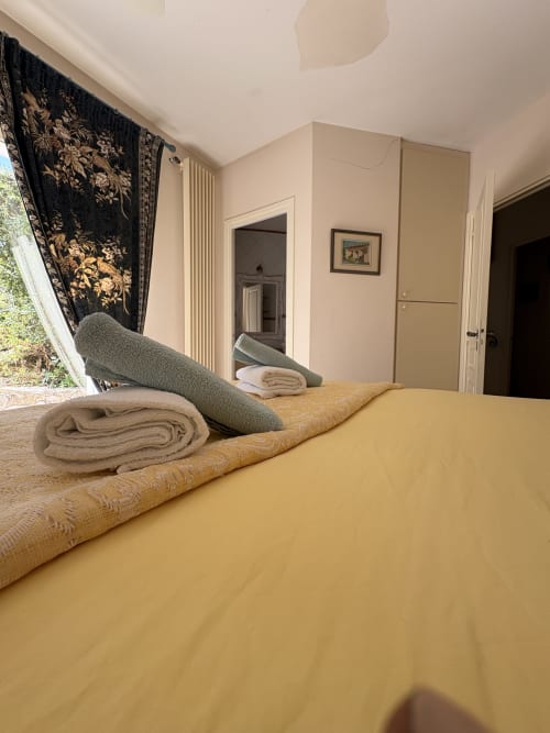 Chambre spacieuse avec literie jaune, tapis roulés et rideaux floraux noirs à la Conciergerie Maurin à Arles