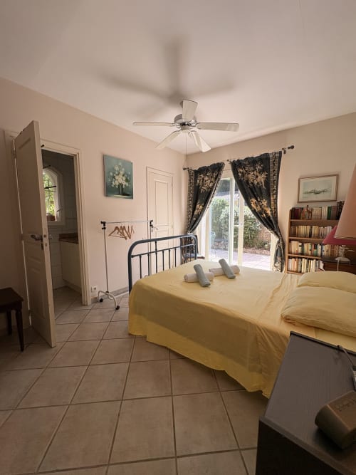 Chambre spacieuse de la Conciergerie Maurin à Arles avec lit jaune, ventilateur de plafond, rideaux épais, bibliothèque et accès à la terrasse