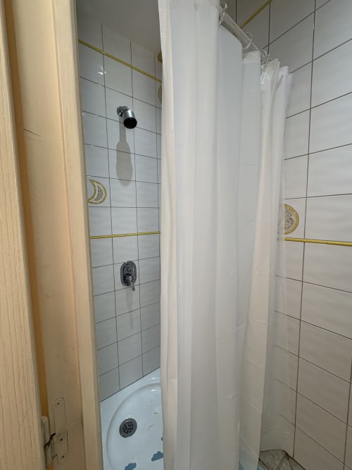 Salle de bain moderne avec douche aux rideaux blancs, carrelage mural et robinetterie chromée à la Conciergerie Maurin à Arles
