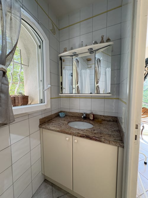 Salle de bain moderne avec comptoir en granit, mobilier blanc et miroir dans une chambre de l'hôtel Conciergerie Maurin, Arles