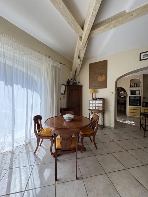 Salle à manger du Paradis du Paradou à la Conciergerie Maurin, Arles, avec table ronde en bois, chaises rembourrées et poutres apparentes