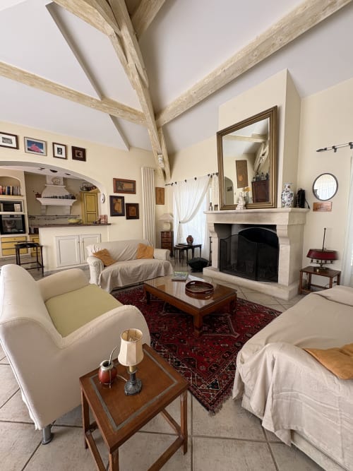 Élégant salon de la Conciergerie Maurin à Arles avec mobilier crème, poutres apparentes, cheminée et décor d'époque