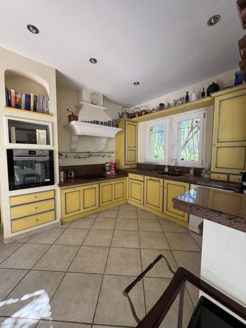 Cuisine jaune vif aux murs crème, plan de travail foncé, électroménagers inox et carrelage à la Conciergerie