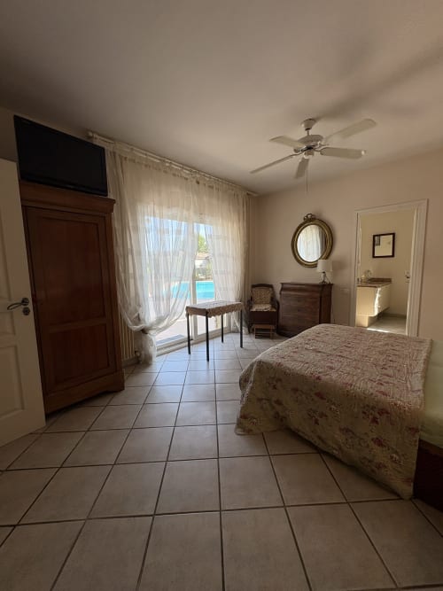 Chambre spacieuse avec vue sur la piscine à la Conciergerie Maurin, Arles. Lit, ventilateur, portes-fenêtres vers terrasse.