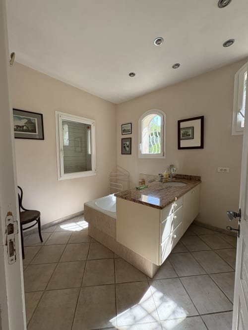 Salle de bain spacieuse à la Conciergerie Maurin à Arles avec vasque blanche, plan de travail en granit, baignoire îlot et grandes fenêtres