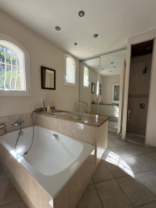 Salle de bain spacieuse à la Conciergerie Maurin à Arles avec baignoire, plan de travail en granit, miroir et douche