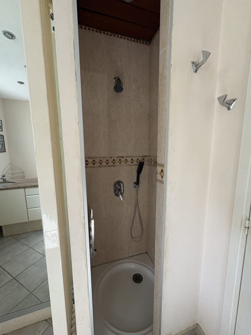 Douche moderne avec carrelage taupe, frise décorative, pommeau de douche pluie et douchette dans chambre d'hôtel
