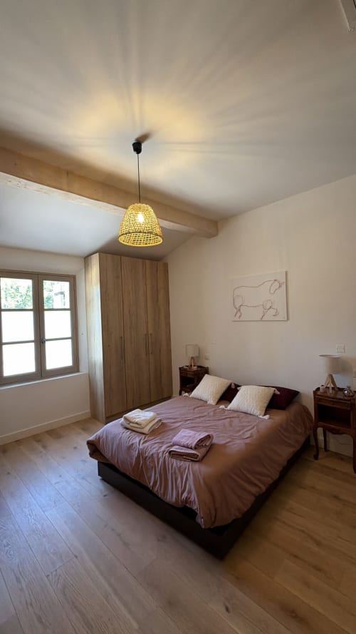 Chambre spacieuse au Mas en Camargue à Arles avec lit double, armoire en bois, lampe suspendue et vue sur le jardin