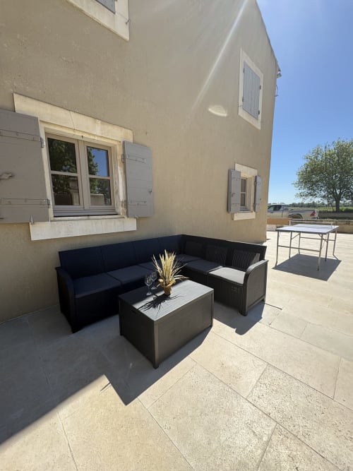Terrasse extérieure du Mas en Camargue à Arles avec canapé sectionnel gris, table basse et mobilier de salle à manger sur patio pavé