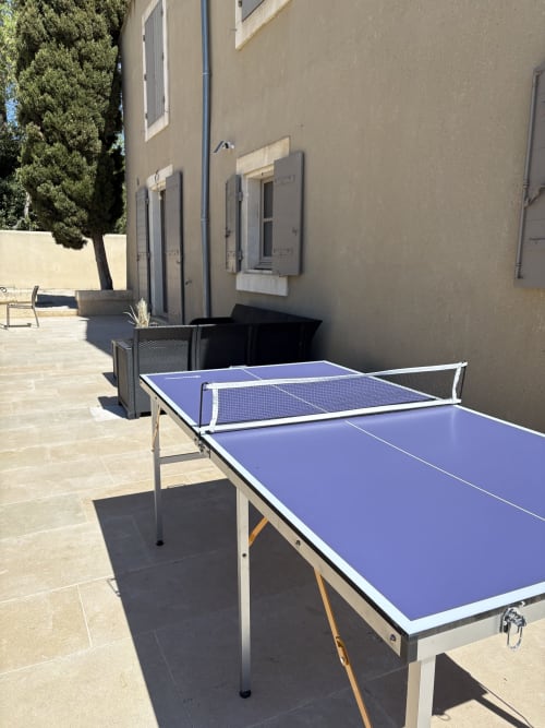 Table de ping-pong ensoleillée sur la terrasse de la Conciergerie Maurin à Arles, avec bâtiment en pierre et cyprès