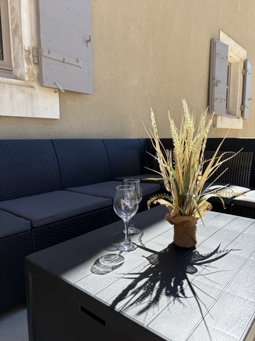 Salon extérieur de la Conciergerie Maurin avec canapé bleu marine, verre de vin et compositions de blé sec à Arles