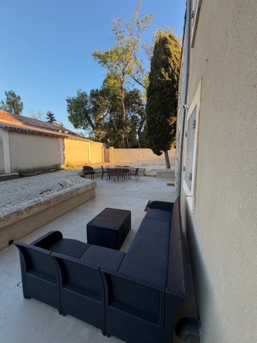 Terrasse extérieure avec mobilier en rotin, table à manger et foyer à la Conciergerie Maurin à Arles, avec un grand cyprès