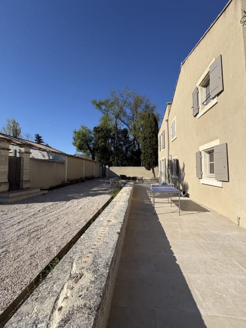 Cour ensoleillée de la Conciergerie Maurin à Arles avec terrasse, jardin de gravier et bâtiment Mas couleur crème