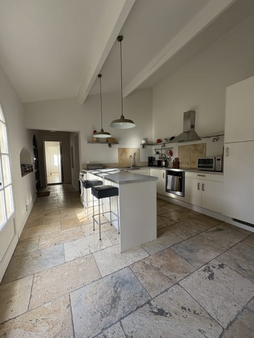 Cuisine contemporaine avec meubles blancs, îlot, luminaires suspendus et carrelage pierre au Gité Château de Pannis, Arles