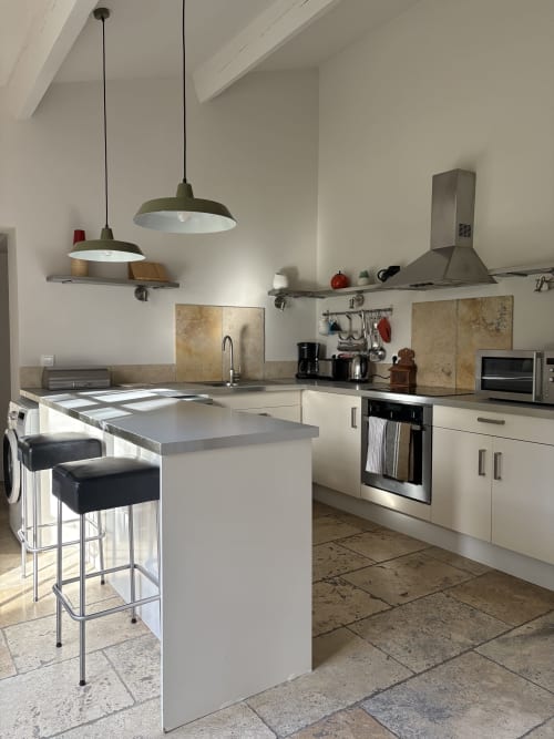 Cuisine moderne avec îlot, luminaires suspendus et appareils inox au Gîte château de Pannis à Arles