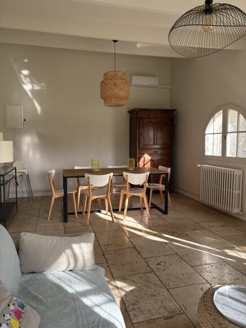 Salle à manger lumineuse du Gité Château de Pannis à Arles avec table en bois, suspension tissée et vue sur le jardin par arcades