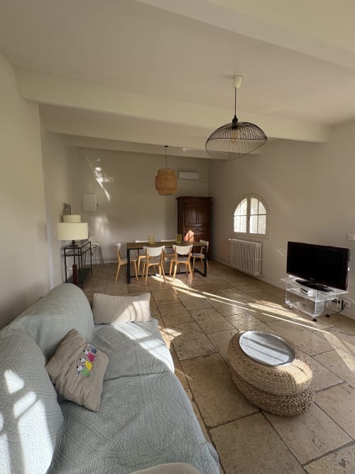 Spacieux séjour ouvert au Gite Chateau de Pannis à Arles avec canapé, table à manger, TV et vue sur le jardin par baies vitrées