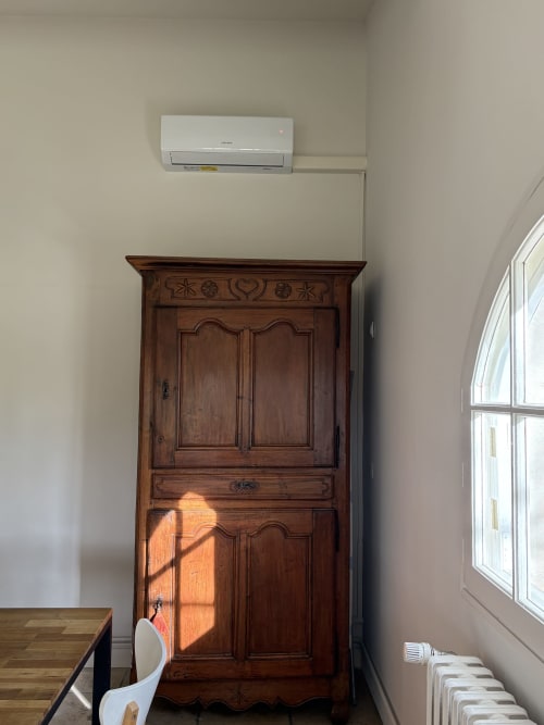 Armoire en bois sculpté baignée de lumière naturelle au Gîte château de Pannis à Arles, avec climatiseur mural au-dessus