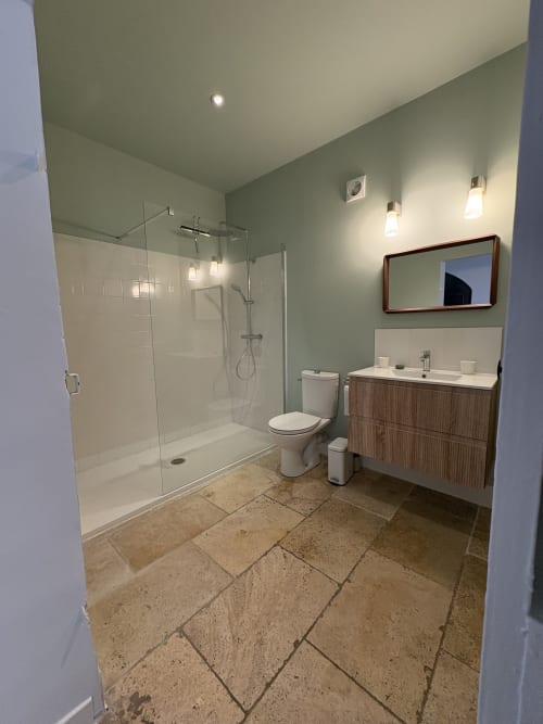 Salle de bain moderne avec douche vitrée, vasque, toilettes et carrelage travertin au Gîte château de Pannis à Arles